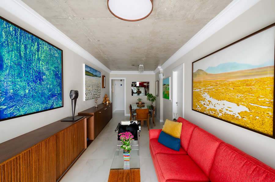 Na sala de estar, o sofá vermelho foi posicionado para criar uma harmonia entre as obras de arte e a marcenaria planejada | Projeto da Trees Arquitetura | Foto: Ricardo Abreu