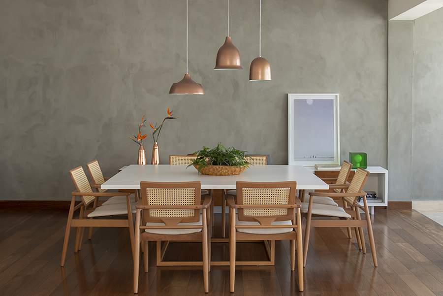Na sala de jantar projetada pela arquiteta Patricia Miranda, &agrave; frente do escrit&oacute;rio Ra&iacute;zes Arquitetos, o rodap&eacute; configurou-se como um prolongamento do piso de madeira. A combina&ccedil;&atilde;o resultou em uma apar&ecirc;ncia harm&ocirc;nica que manteve a uniformidade do material e promoveu um sutil contraste com o efeito de cimento queimado na parede | Foto: Cac&aacute; Bratke | Produ&ccedil;&atilde;o: Debbie Apsan