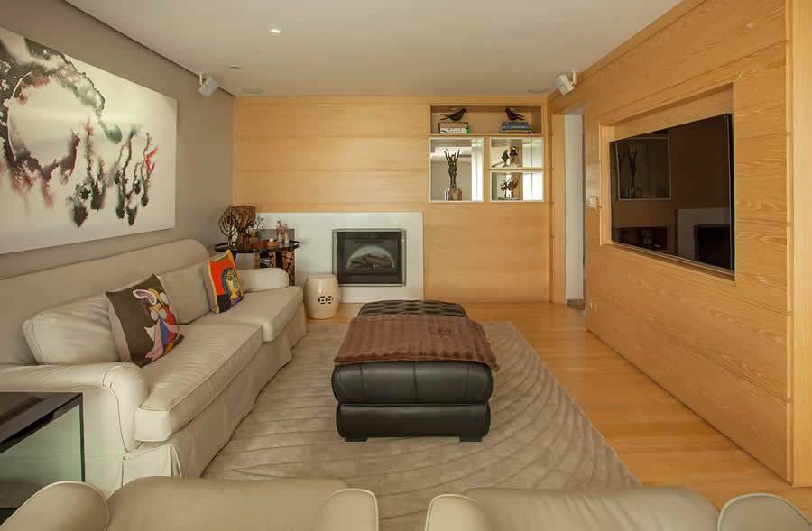 Nesta sala de TV, Karina Korn adotou um painel de madeira em toda a extens&atilde;o das paredes, inclusive onde est&aacute; a lareira, trazendo conforto visual ao ambiente. A op&ccedil;&atilde;o foi criar um nicho na marcenaria para embutir levemente a tela | Foto: Eduardo Pozella