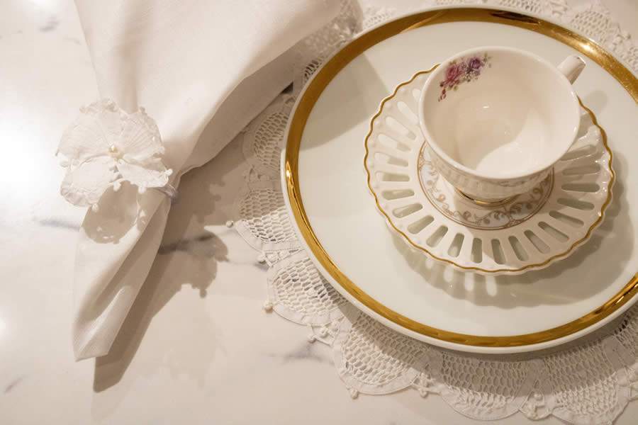 Mesa posta com renda Renascença, louças em porcelanas brancas com dourado, faqueiro, taças e peças decorativas - Virgínia Brandão