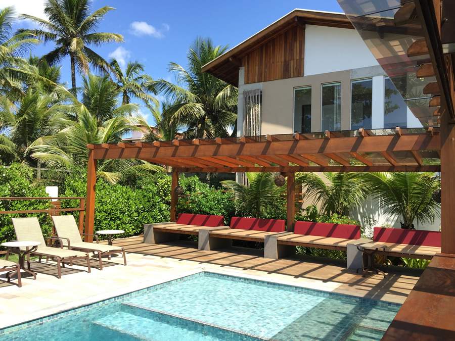  Cezar Scarpato optou por um pergolado para trazer um sombreamento parcial ao lounge ao redor da piscina, que recebeu chaises sob medida em courvin n&aacute;utico. A estrutura, feita de madeira aparelhada com cobertura de vidro temperado laminado e pel&iacute;cula refletiva, tamb&eacute;m serve como passagem coberta para a &aacute;rea do bar. Foto: Bicubico