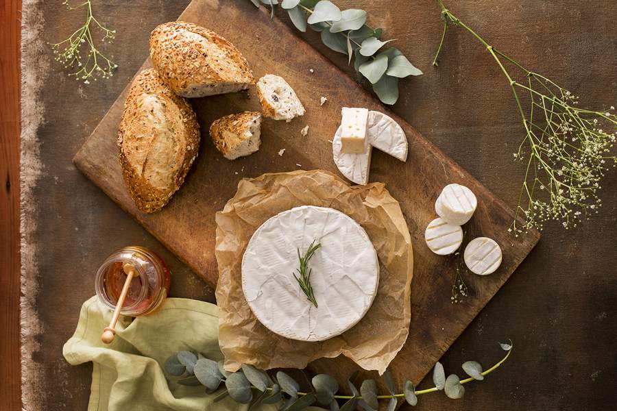T&aacute;bua de queijos com diferentes cortes de Brie servidos com p&atilde;es, ervas finas e mel