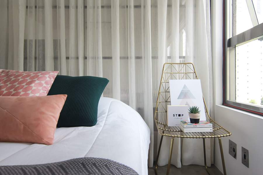 No apto com conceito MaxHaus, as arquitetas Eduarda Negretti e Nathalia Lena, do Lene Arquitetos, dividiram a &aacute;rea social da &iacute;ntima com uma serralheria e cortina, que propicia privacidade, quando necess&aacute;rio. Para decorar o cantinho na lateral da cama, a cadeira recebe os quadros preferidos dos moradores l Foto: Luciano Sessa