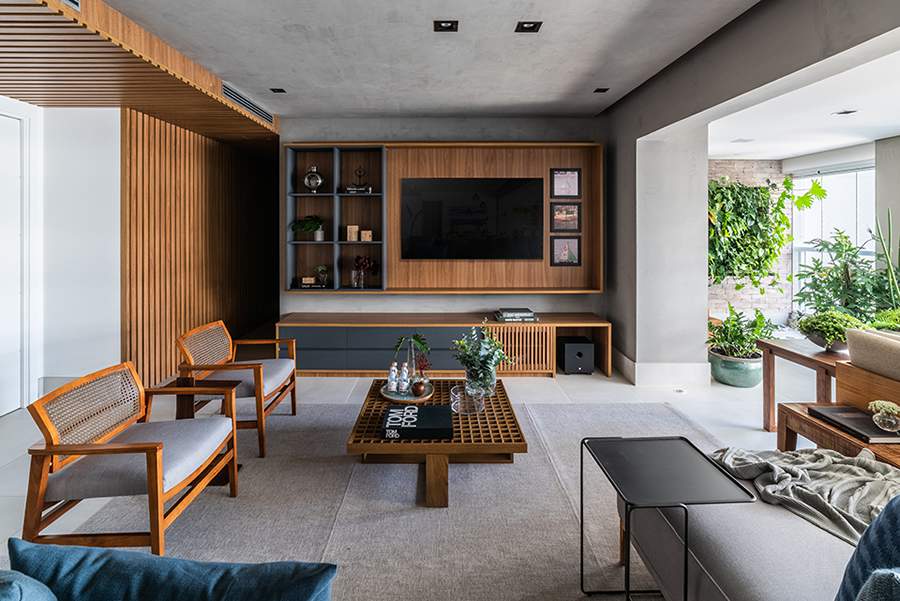 Nesta sala projetada pelo arquiteto Pietro Terlizzi, o acinzentado do efeito do cimento queimado tornou-se a base para a presen&ccedil;a aconchegante da madeira &ndash; presente no efeito ripado das paredes, o forro no teto que camufla o ar-condicionado, o painel da TV e o mobili&aacute;rio | Foto: Guilherme Pucci