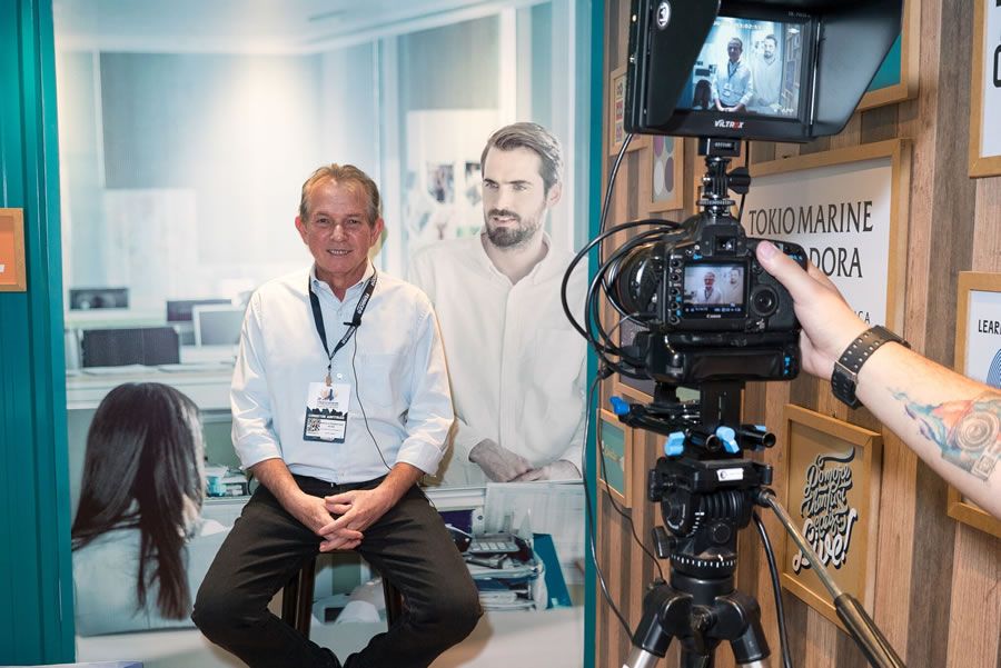 Corretor no estande da Tokio Marine, gravando vídeo