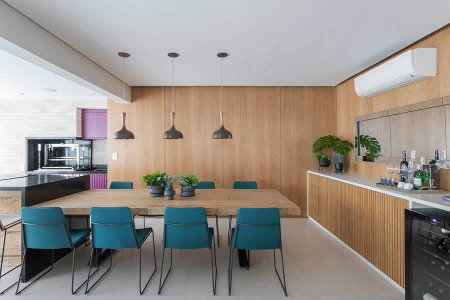 O verde das cadeiras de jantar e o f&uacute;csia na marcenaria da churrasqueira d&atilde;o um toque ousado &agrave; &aacute;rea social. Nas paredes, os pain&eacute;is de carvalho americano cuidam de trazer a sensa&ccedil;&atilde;o de aconchego aos ambientes | Foto: Thiago Travesso