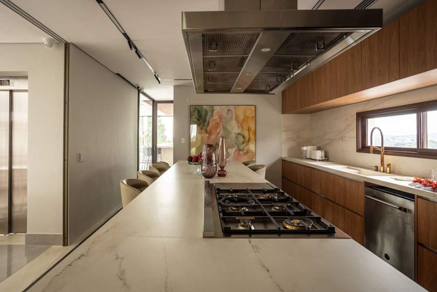 Coifas e depuradores merecem atenção especial nos projetos de arquitetura de interiores. Ainda mais em uma cozinha aberta, ninguém quer que gordura e odores se espalhem para os outros cômodos. Nesse projeto, os arquitetos Mariana Meneghisso e Alexandre Pasquotto definiram um modelo potente de coifa, acompanhando a robustez do cooktop instalado na bancada | Projeto Meneghisso &amp; Pasquotto Arquitetura | Foto: JP Image