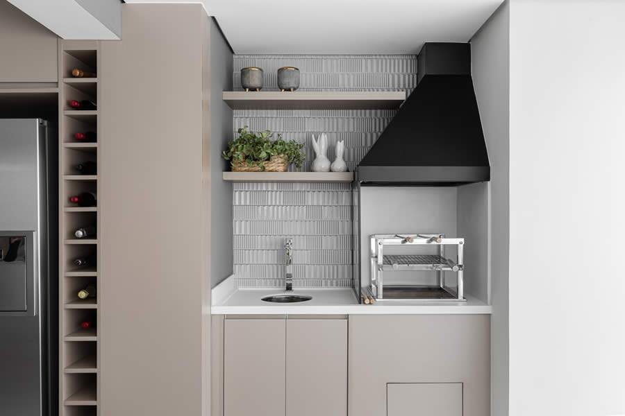 Na varanda gourmet deste apartamento, a churrasqueira com braseiro e carv&atilde;o &eacute; parte integrante da estrutura do ambiente com ampla bancada, pia e arm&aacute;rios. Uma divis&oacute;ria de vidro protege de respingos de gordura | Foto: Gisele Rampazzo