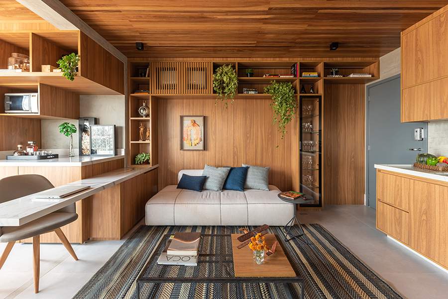 Na sala de estar projetada por Pietro Terlizzi, a madeira &eacute; protagonista e est&aacute; em forro (cumaru), paredes e mobili&aacute;rio de freij&oacute;. O material tamb&eacute;m serve de base para a bancada flutuante, d&aacute; forma aos nichos, prateleiras, cristaleira e esconde o ar-condicionado | Foto: Guilherme Pucci