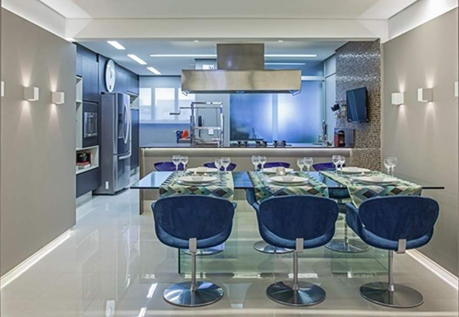 No apartamento de uma moradora que adora receber familiares e amigos, a arquiteta Cristiane Schiavoni n&atilde;o teve d&uacute;vidas: com a cozinha aberta &ndash; com direito &agrave; ilha com cooktop &ndash;, a proximidade com mesa de jantar foi perfeita para os momentos de confraterniza&ccedil;&atilde;o. Em destaque o azul das cadeiras estofadas no entorno da mesa &lsquo;dialogam&rsquo; com as banquetas, da mesma cor, em acr&iacute;lico| Foto: Carlos Piratininga